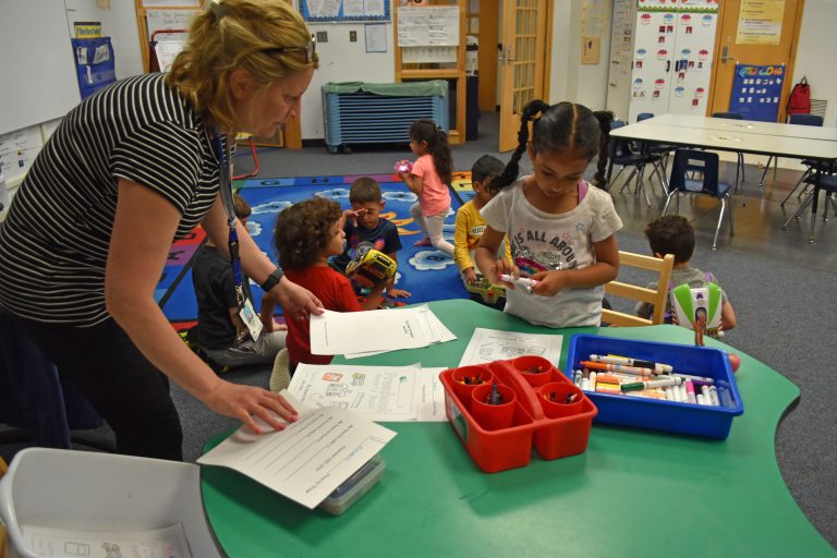 A teacher works with a young student learning to write her name.